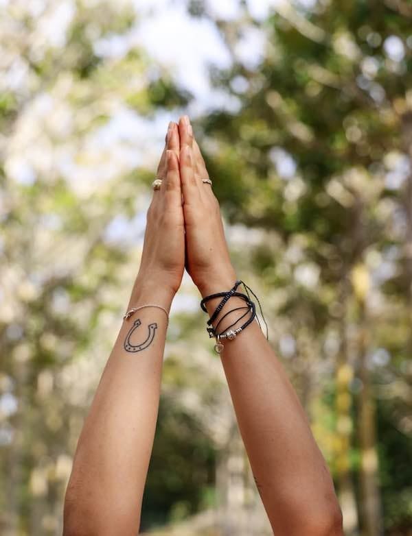 A person with their hands over their head with the palms touching each other while outside.